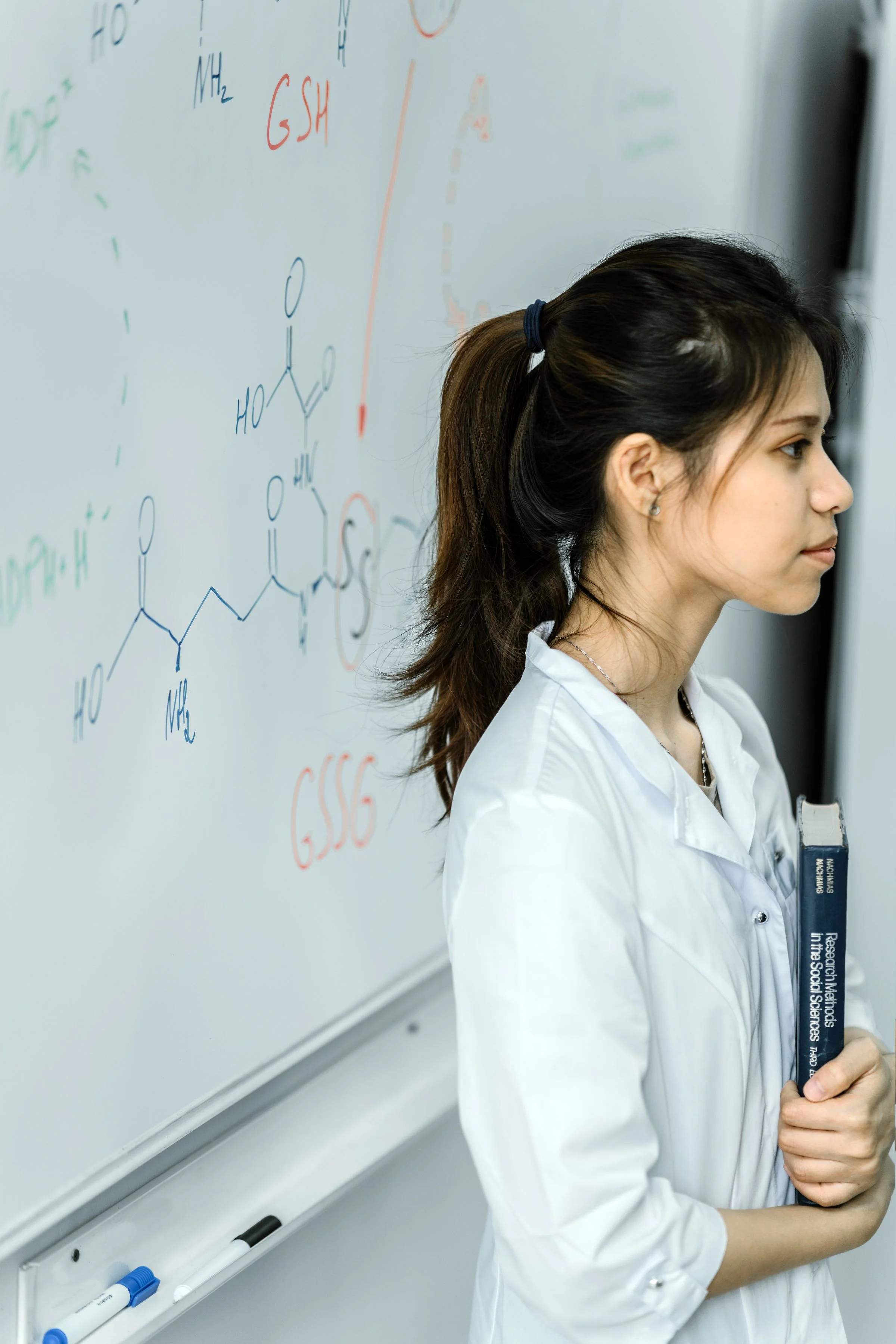A teacher beside a whiteboard covered in chemical structures.