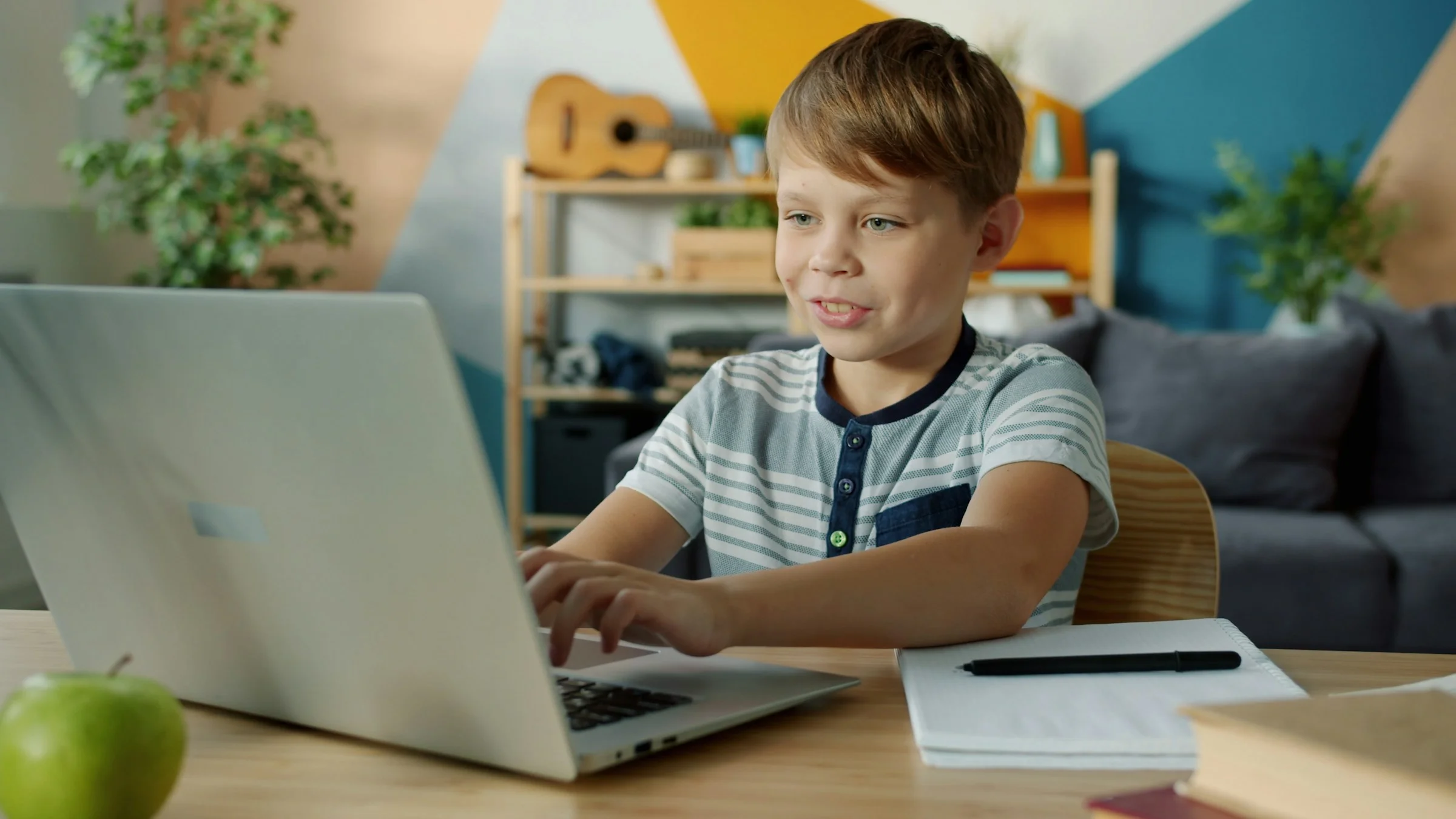 A boy smiling as he works at his laptop during an online lesson