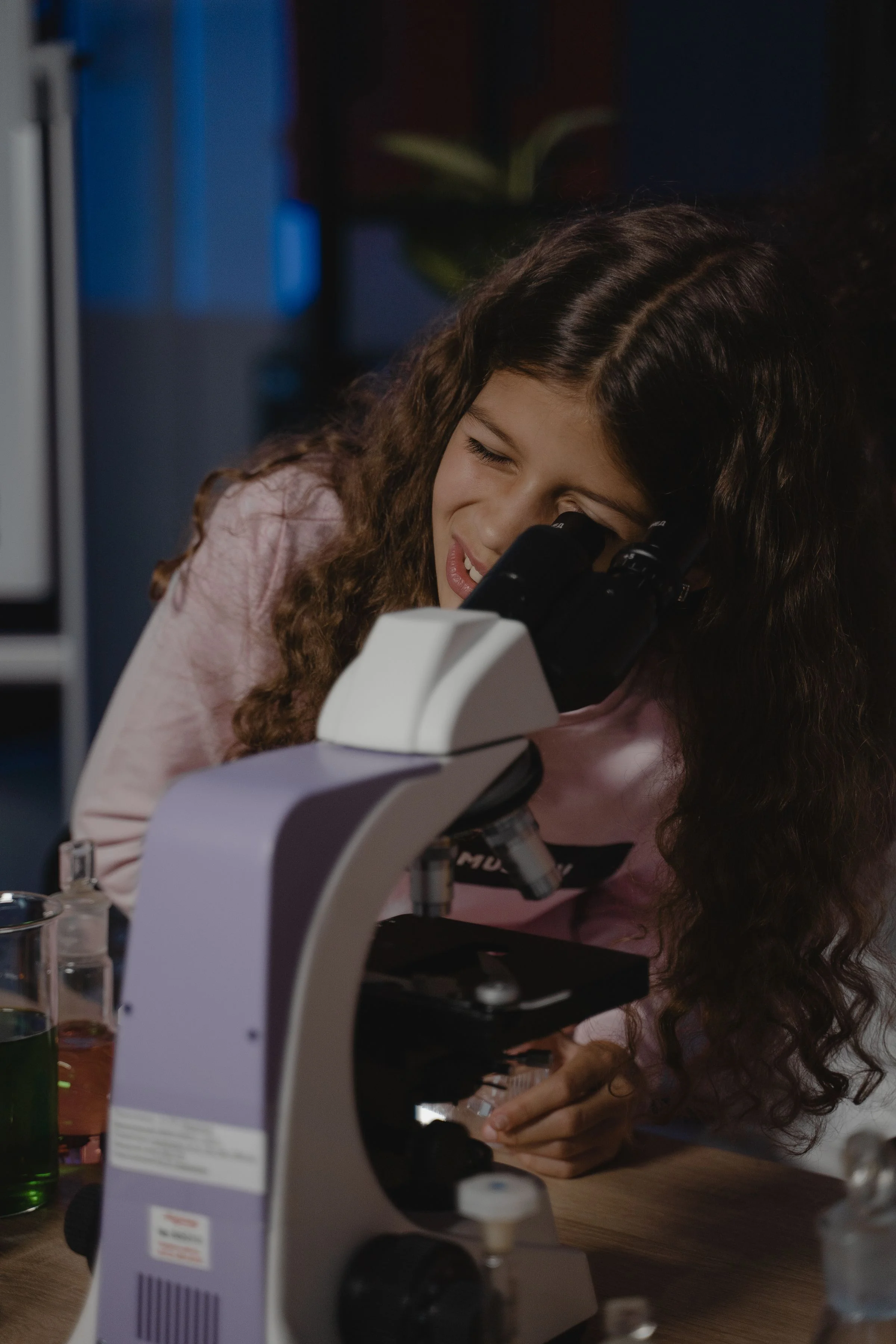A student smiling as she looks into a microscope.