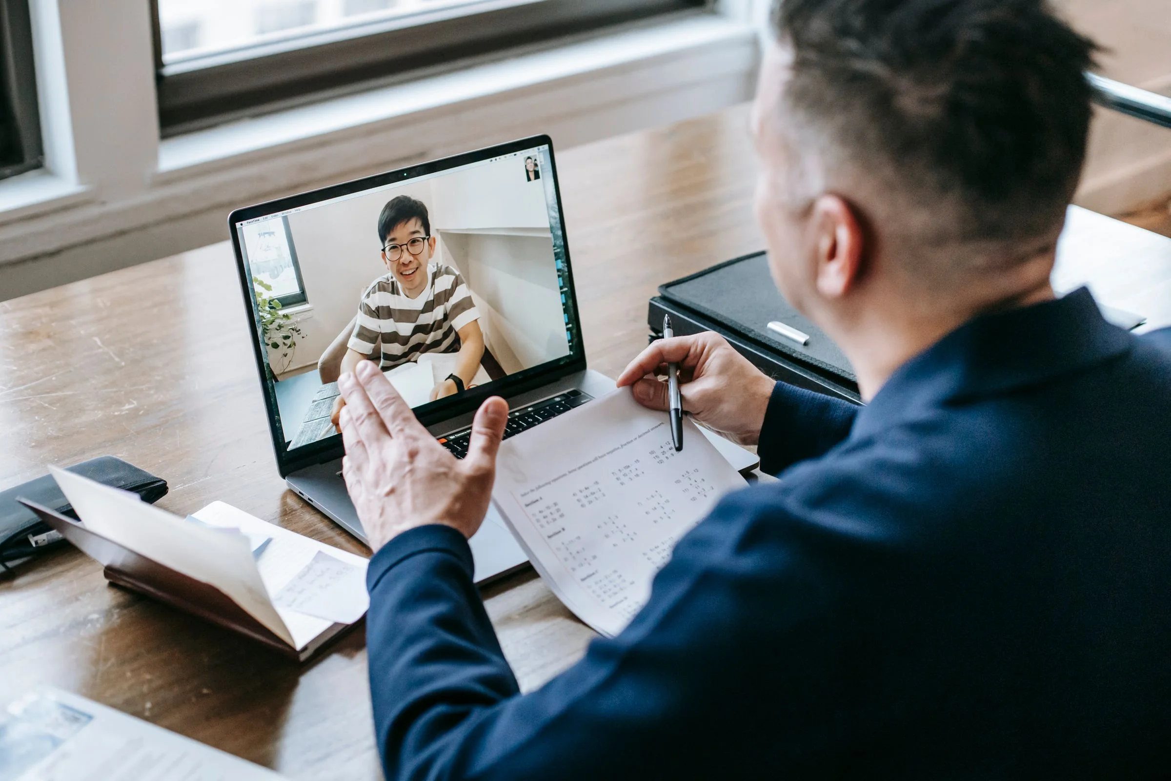 A tutor holding a worked example up to the student on his laptop screen.