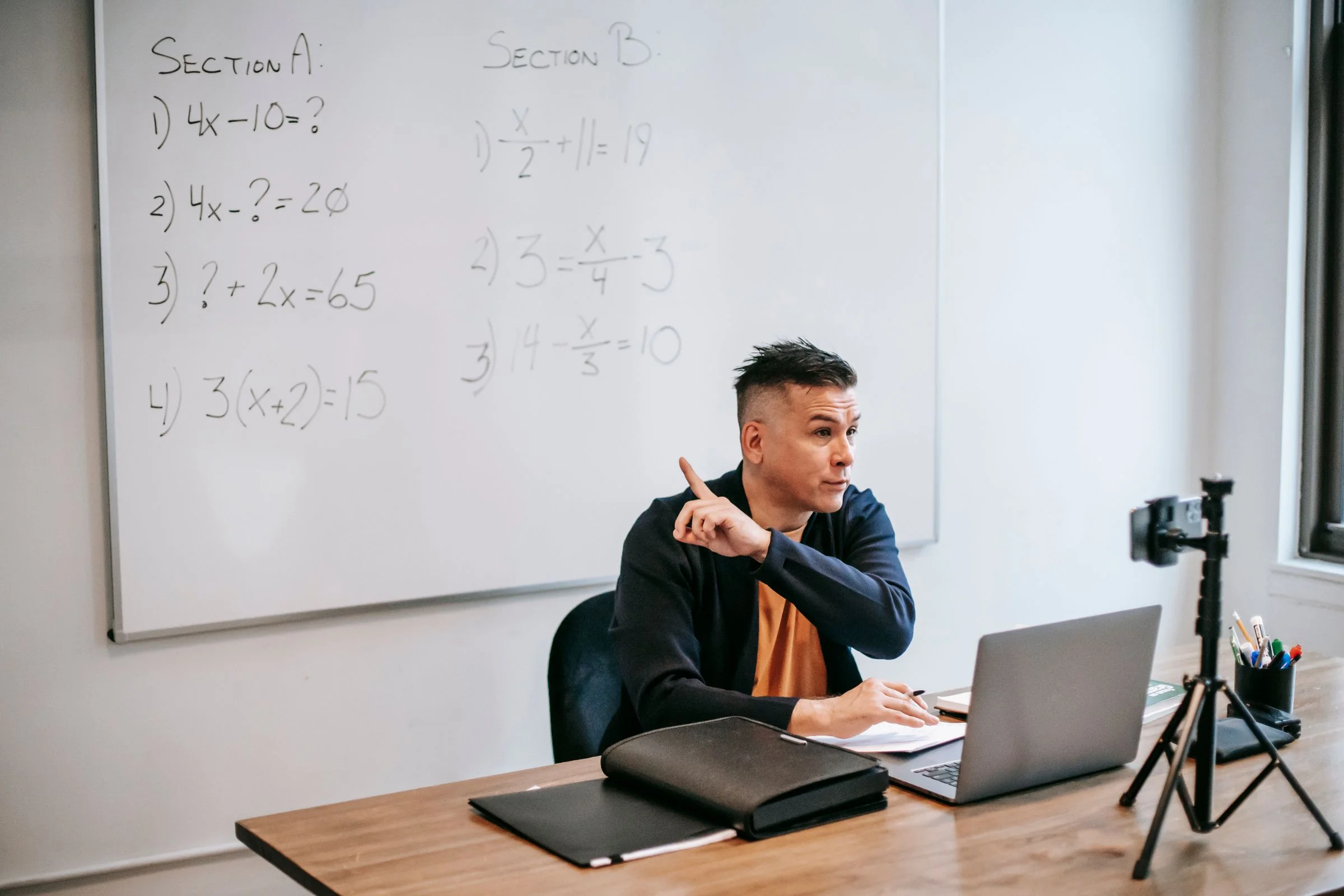A tutor pointing through a worked equation on the whiteboard during an online lesson.